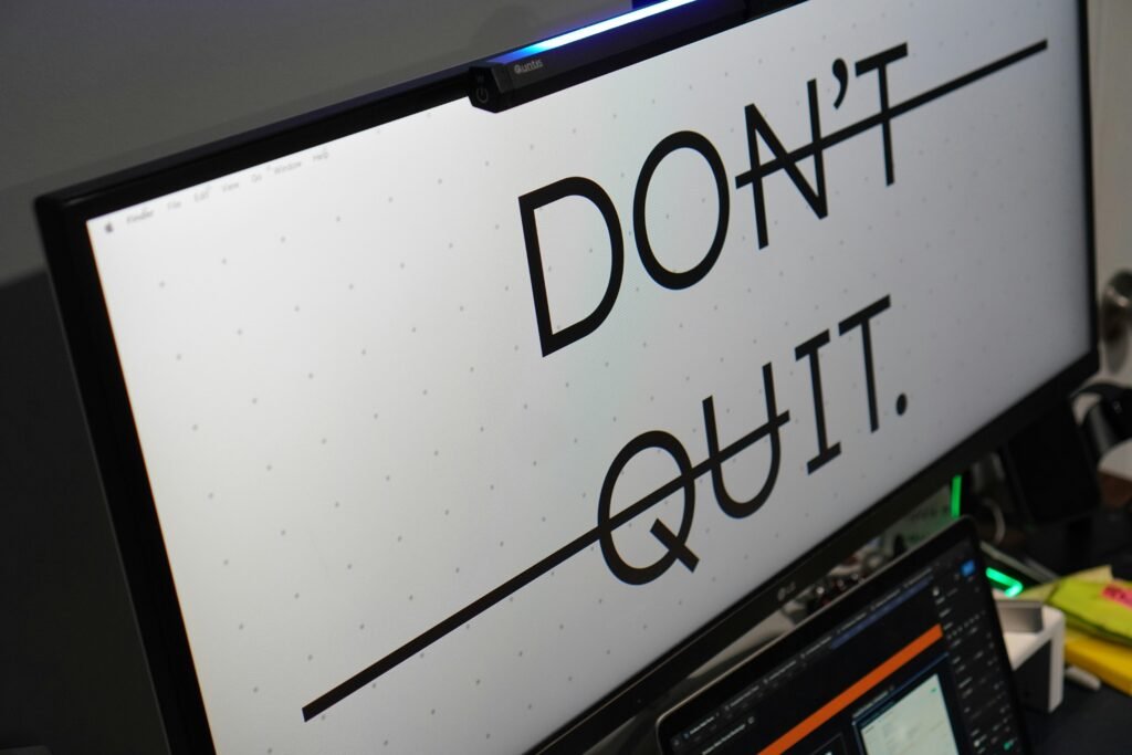 Ein Computerbildschirm zeigt den Text 'don't quit.' auf dunklem Hintergrund, Schreibtisch im modernen Büro