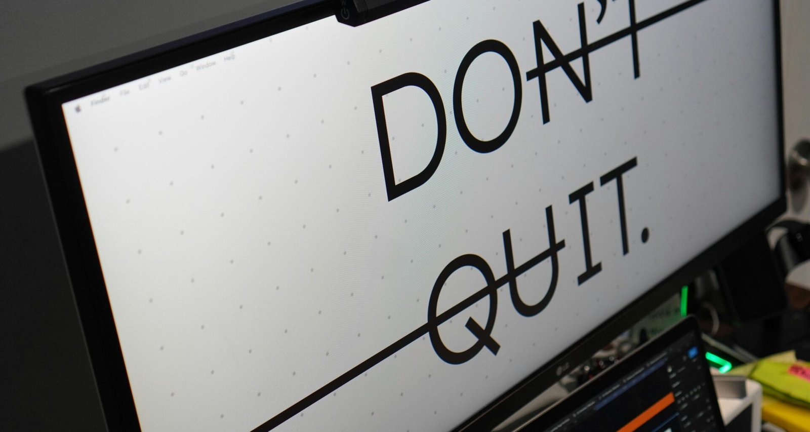 Ein Computerbildschirm zeigt den Text 'don't quit.' auf dunklem Hintergrund, Schreibtisch im modernen Büro