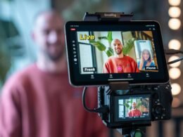 Kamera filmt einen Live-Videoanruf mit zwei Personen auf einem Bildschirm in einem modernen Arbeitsumfeld.