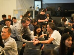 Mehrere Menschen in einem modernen Raum, einige führen Unterhaltungen und tauschen sich aus, andere stehen zusammen.