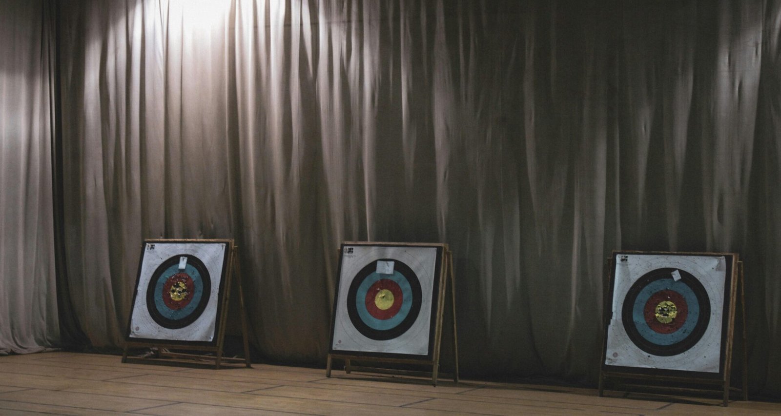 Drei farbige Bogenschieß-Zielscheiben stehen nebeneinander vor einem hellen Vorhang in einer Sporthalle.