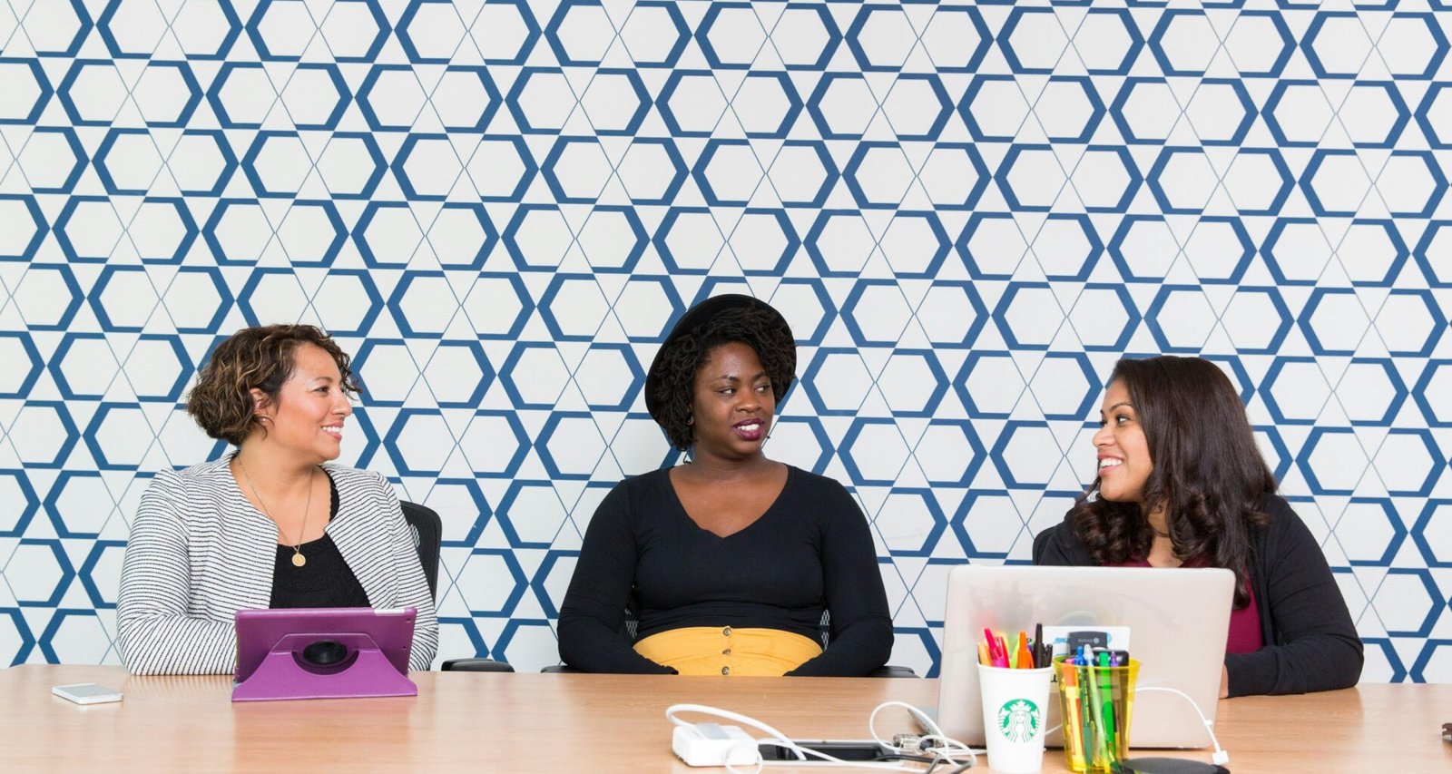 Drei Frauen sitzen nebeneinander auf Stühlen vor einem Tisch und besprechen gemeinsam Arbeitsunterlagen im Büro.