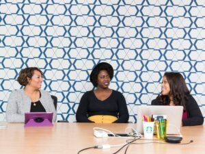 Drei Frauen sitzen nebeneinander auf Stühlen vor einem Tisch und besprechen gemeinsam Arbeitsunterlagen im Büro.