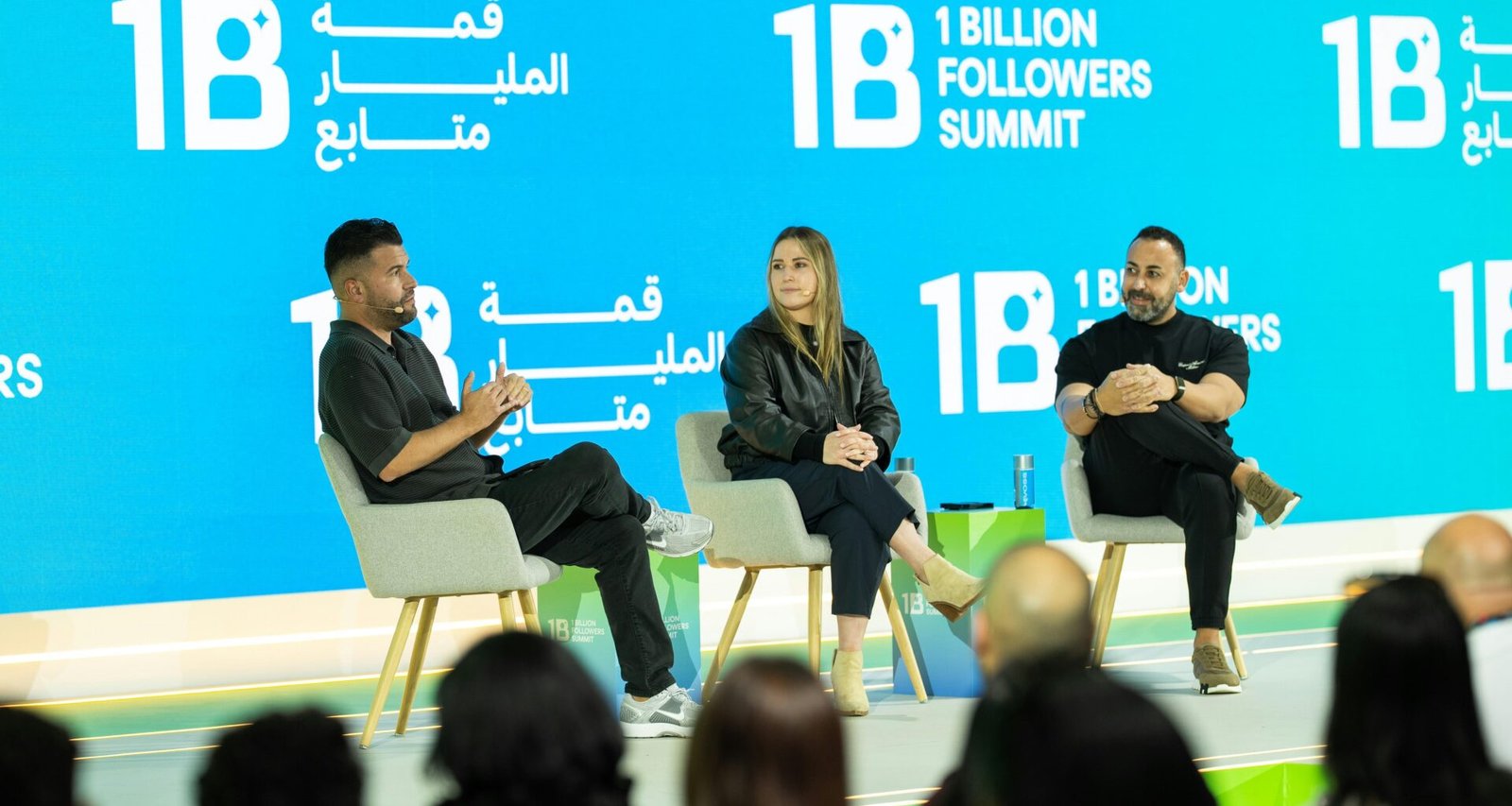 Drei Personen präsentieren auf einer Konferenzbühne und sprechen vor Publikum beim Summit