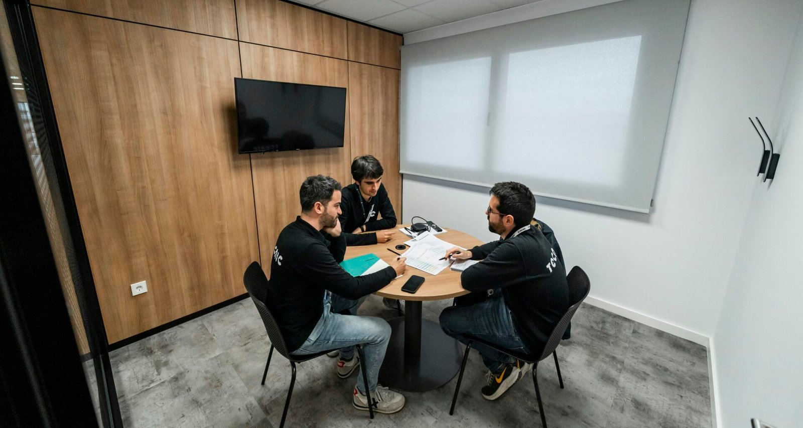 Drei Personen sitzen an einem Tisch in einem hellen Konferenzraum und besprechen Projekte während eines Meetings.
