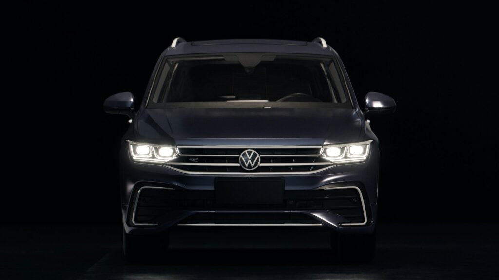 Dunkelblauer Volkswagen SUV mit leuchtenden Frontscheinwerfern auf Straße bei Dämmerung, moderner Look