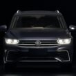 Dunkelblauer Volkswagen SUV mit leuchtenden Frontscheinwerfern auf Straße bei Dämmerung, moderner Look