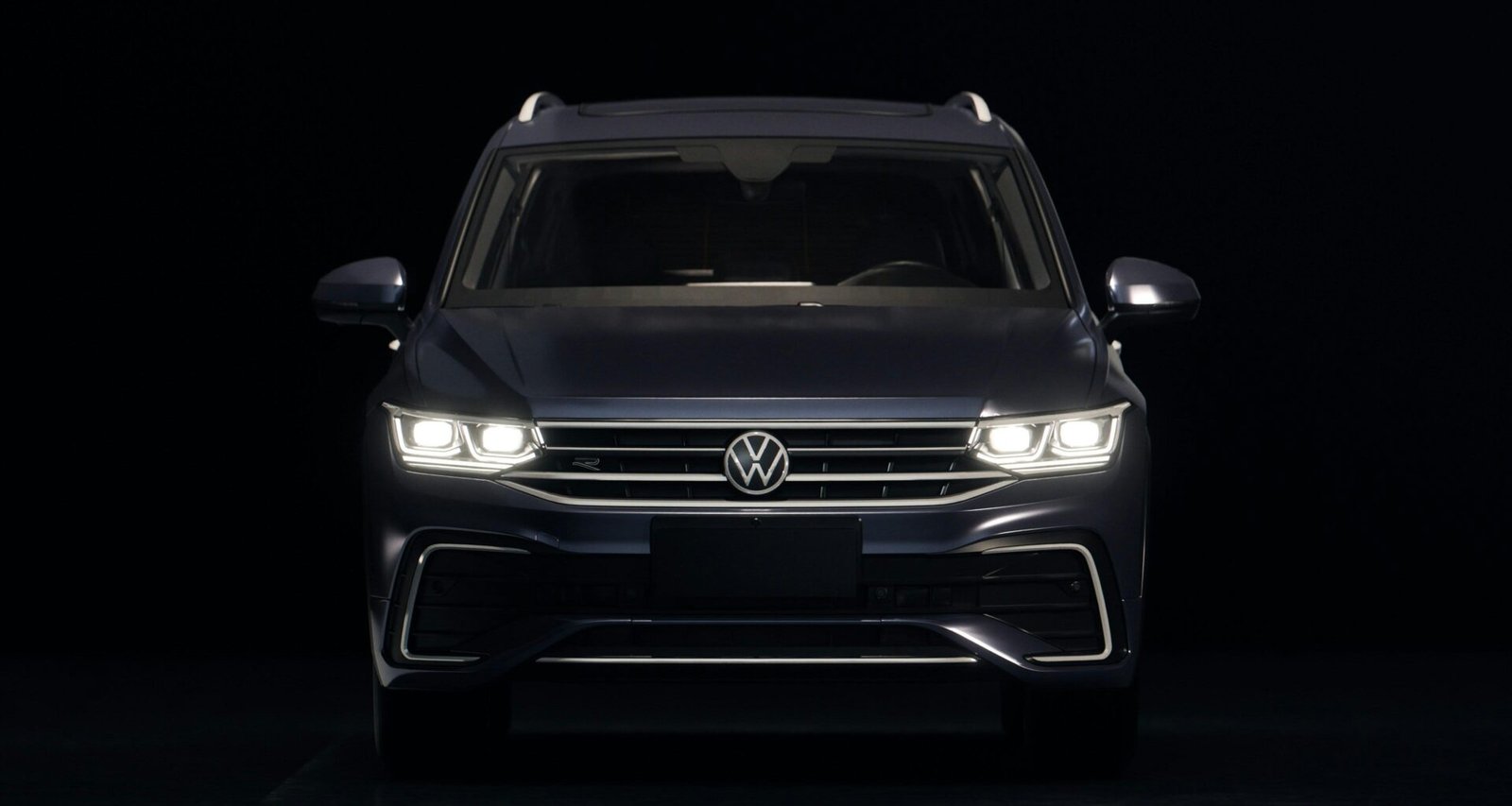 Dunkelblauer Volkswagen SUV mit leuchtenden Frontscheinwerfern auf Straße bei Dämmerung, moderner Look