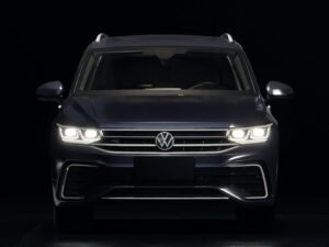 Dunkelblauer Volkswagen SUV mit leuchtenden Frontscheinwerfern auf Straße bei Dämmerung, moderner Look