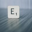 Scrabble-Stein mit der Aufschrift E1 liegt auf einer hellen Holzoberfläche, als Symbol für Ideen im Online-Marketing.