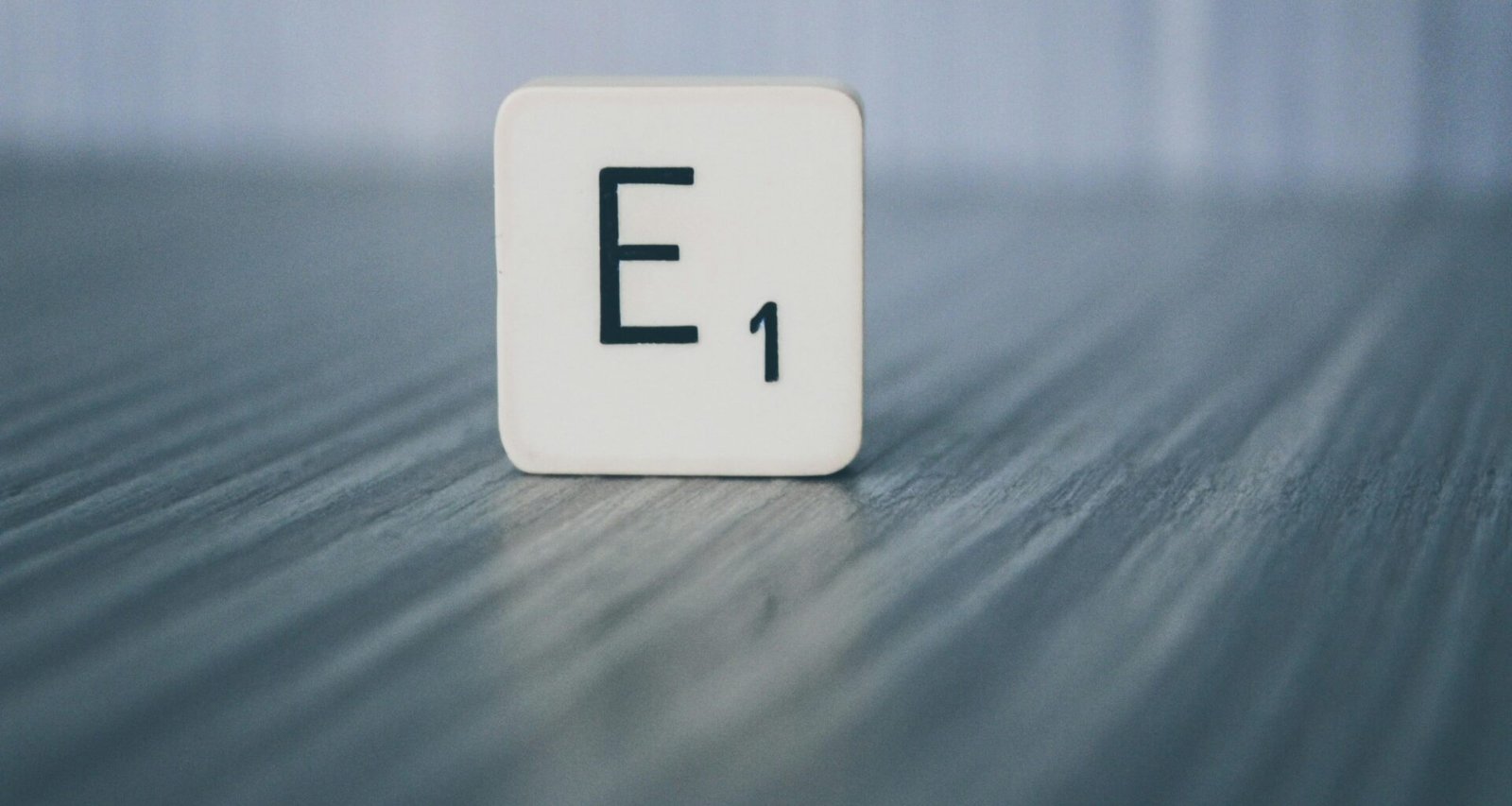 Scrabble-Stein mit der Aufschrift E1 liegt auf einer hellen Holzoberfläche, als Symbol für Ideen im Online-Marketing.