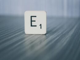 Scrabble-Stein mit der Aufschrift E1 liegt auf einer hellen Holzoberfläche, als Symbol für Ideen im Online-Marketing.