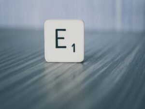 Scrabble-Stein mit der Aufschrift E1 liegt auf einer hellen Holzoberfläche, als Symbol für Ideen im Online-Marketing.