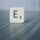 Scrabble-Stein mit der Aufschrift E1 liegt auf einer hellen Holzoberfläche, als Symbol für Ideen im Online-Marketing.