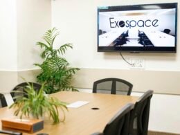 Ein Konferenzraum mit großem Exospace Logo auf dem Bildschirm, moderner Einrichtung und klarer Raumaufteilung.