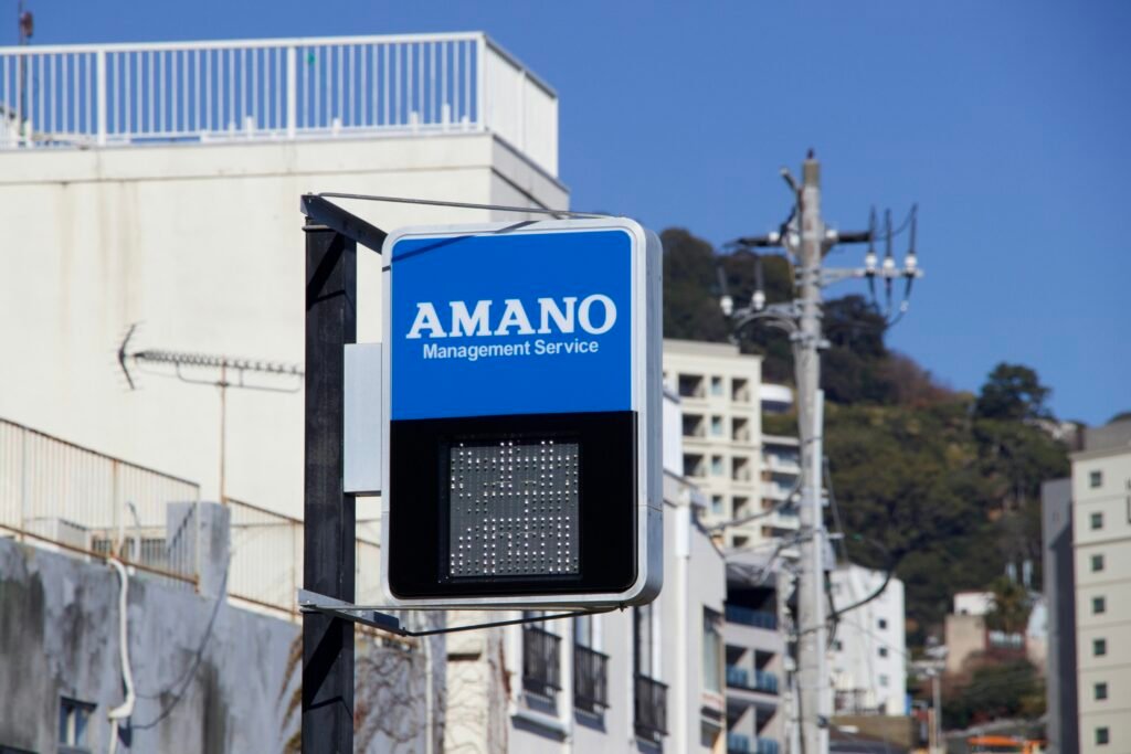 Blaues Schild mit Amano Management Service Logo, fotografiert draußen an einer Gebäudefassade bei Tageslicht