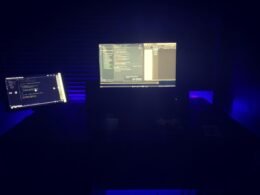 Ein Computermonitor steht auf einem Schreibtisch, umgeben von typischer Büroausstattung