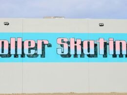 Großes Schild mit der Aufschrift Roller Skating an der Seitenwand eines Gebäudes, fotografiert aus leichter Untersicht