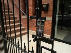 Ein Mobiltelefon ist mit einer Halterung an einem Metallzaun befestigt, fotografiert von Raman Shaunia.