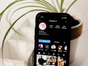 Ein Mobiltelefon liegt auf einem Holztisch neben einer kleinen, grünen Topfpflanze – stilvolles Arrangement für die Arbeitsumgebung.