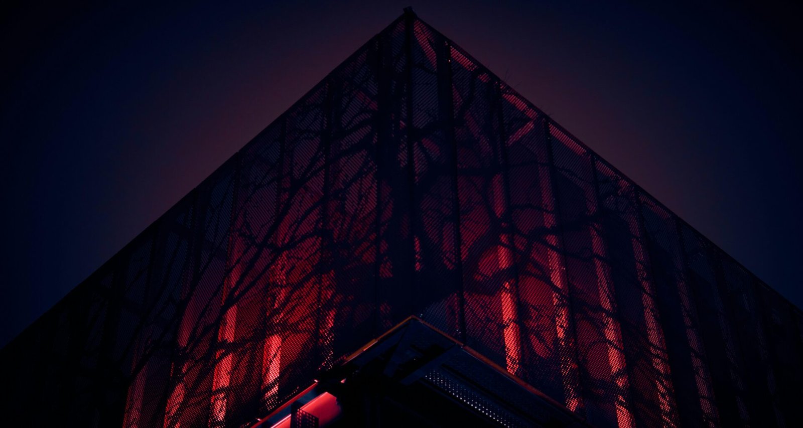 Ein modernes, hohes Gebäude mit rotem Lichtband an der Seitenfassade vor neutralem Himmel.