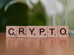 Ein Holzblock mit dem Schriftzug ‚Crypt‘ liegt auf einem Tisch, als Verweis auf Kryptowährungen und digitale Finanzthemen.