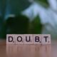 Ein Holzwürfel mit der Aufschrift doubt liegt auf einem Tisch und illustriert das Thema Unsicherheit im Berufsalltag.