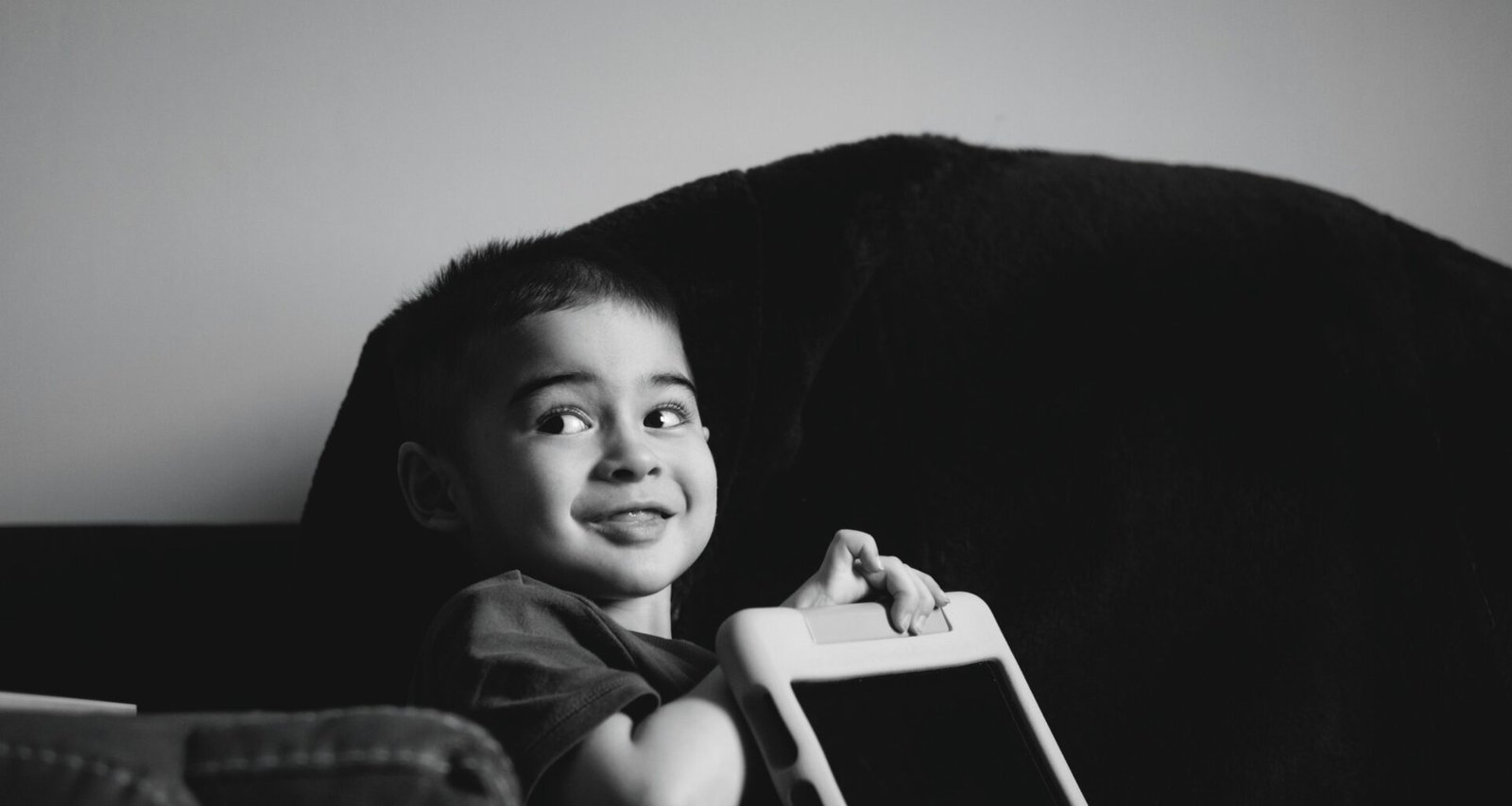 Junger Junge hält lächelnd ein Tablet in den Händen und schaut auf das Display, Symbol für digitale Bildung.