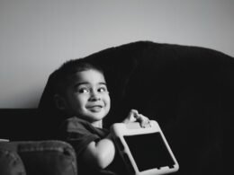 Junger Junge hält lächelnd ein Tablet in den Händen und schaut auf das Display, Symbol für digitale Bildung.