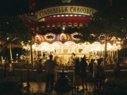 Ein beleuchtetes Karussell bei Nacht, umringt von stehenden Menschen auf einem öffentlichen Platz