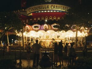 Ein beleuchtetes Karussell bei Nacht, umringt von stehenden Menschen auf einem öffentlichen Platz
