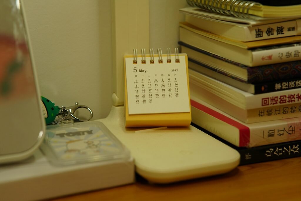 Ein kleiner Tischkalender steht neben einem Stapel Bücher auf einem Schreibtisch, ideal zur Veranschaulichung von Zeitmanagement.