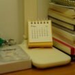 Ein kleiner Tischkalender steht neben einem Stapel Bücher auf einem Schreibtisch, ideal zur Veranschaulichung von Zeitmanagement.