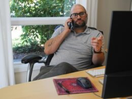 Ein Mann hält sein Smartphone in der Hand und blickt auf den Bildschirm, während er in einem urbanen Umfeld steht.