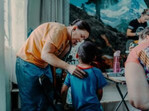 Ein erwachsener Mann steht über einem Jungen, der an einem Tisch sitzt und aufmerksam nach vorne blickt