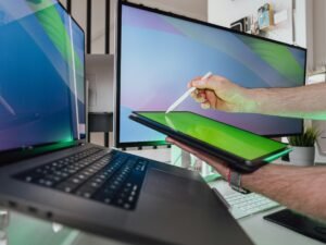 Ein Mann steht vor einem Computerbildschirm und hält einen Laptop in den Händen, Büroarbeitsplatz im modernen Umfeld