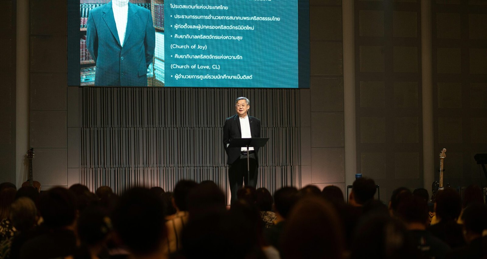 Mann im Anzug spricht am Rednerpult auf einer Konferenz vor einer Gruppe von Zuhörern im Saal.