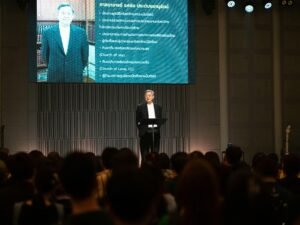 Mann im Anzug spricht am Rednerpult auf einer Konferenz vor einer Gruppe von Zuhörern im Saal.