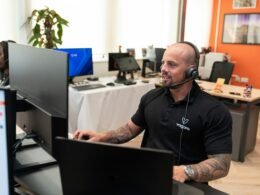 Ein Mann trägt ein Headset und sitzt vor einem Computerbildschirm in einem modernen Büroarbeitsplatz.