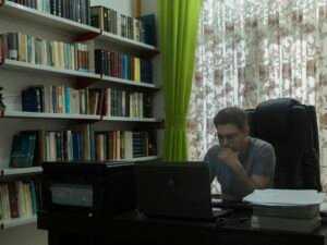 Ein Mann sitzt an einem Schreibtisch vor einem aufgeklappten Laptop und arbeitet konzentriert im Homeoffice.