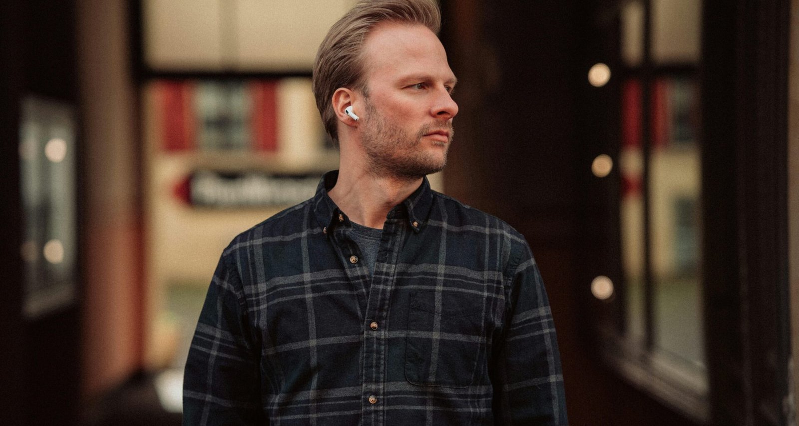 Ein Mann trägt Ohrhörer und steht vor einem großen modernen Gebäude in der Stadt.