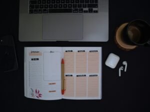 Ein offenes Notizbuch und eine Tasse Kaffee stehen auf einem ordentlich eingerichteten Schreibtisch in moderner Umgebung.