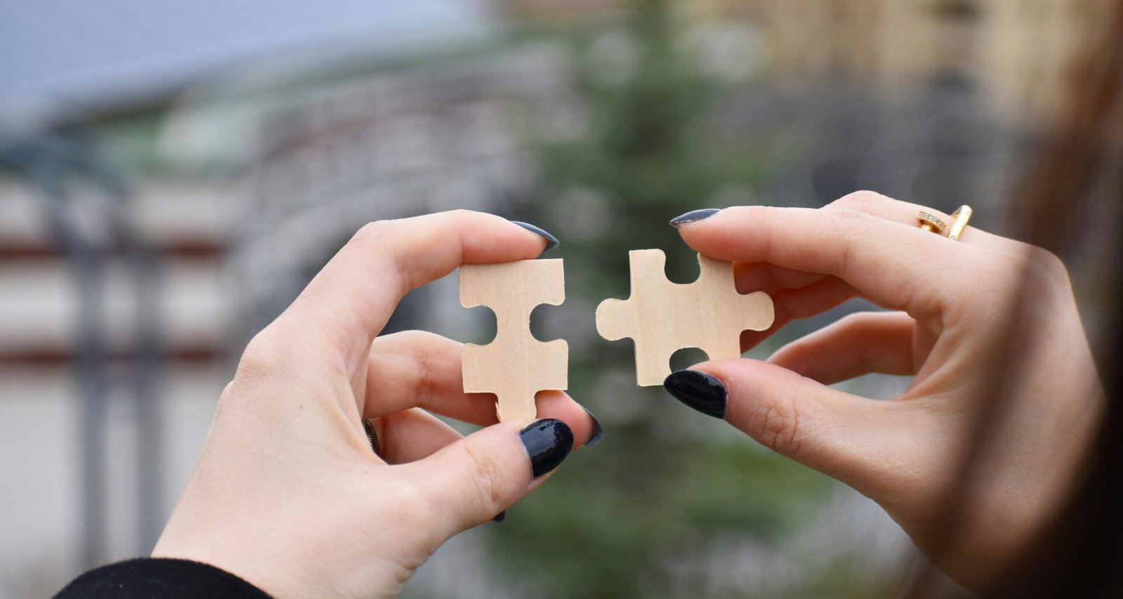 Verschiedene Hände halten gemeinsam ein kleines, weißes Objekt, Close-up-Aufnahme als Symbol für Teamarbeit.