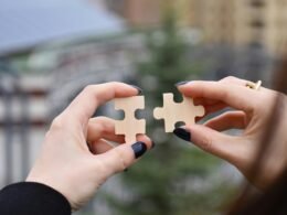 Verschiedene Hände halten gemeinsam ein kleines, weißes Objekt, Close-up-Aufnahme als Symbol für Teamarbeit.