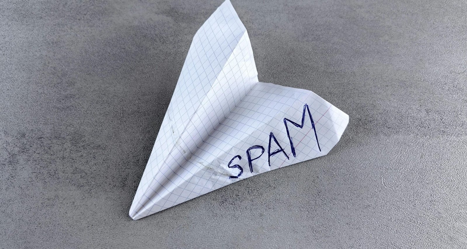 Papierflieger mit dem handgeschriebenen Wort Spam als Sinnbild für unerwünschte E-Mail-Kommunikation