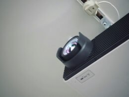 Projektor steht auf einer weißen Wand, bereit für den Einsatz bei Präsentationen und Meetings im Büro oder Homeoffice.