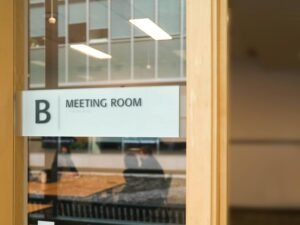 Ein Schild mit der Aufschrift Meeting Room an einer Glastür in einem modernen Bürogebäude als Hinweis auf einen Besprechungsraum