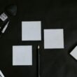 Schwarzer Tisch, auf dem mehrere weiße Karten und ein Bleistift ordentlich arrangiert liegen