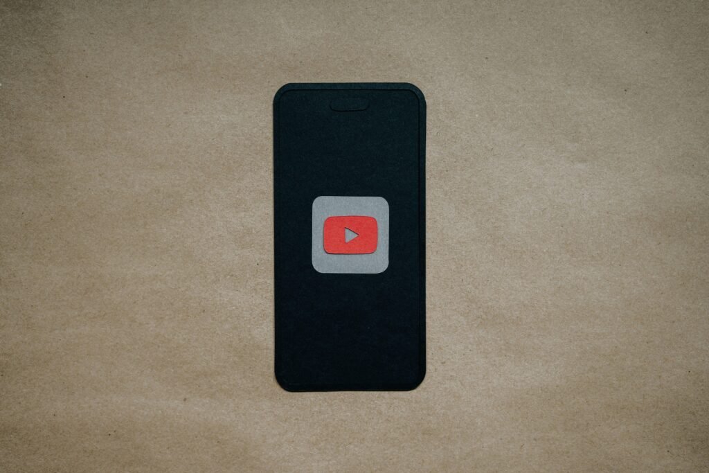 Schwarzes Smartphone mit prominentem roten YouTube-Logo auf dem Display, auf dunklem Hintergrund liegend
