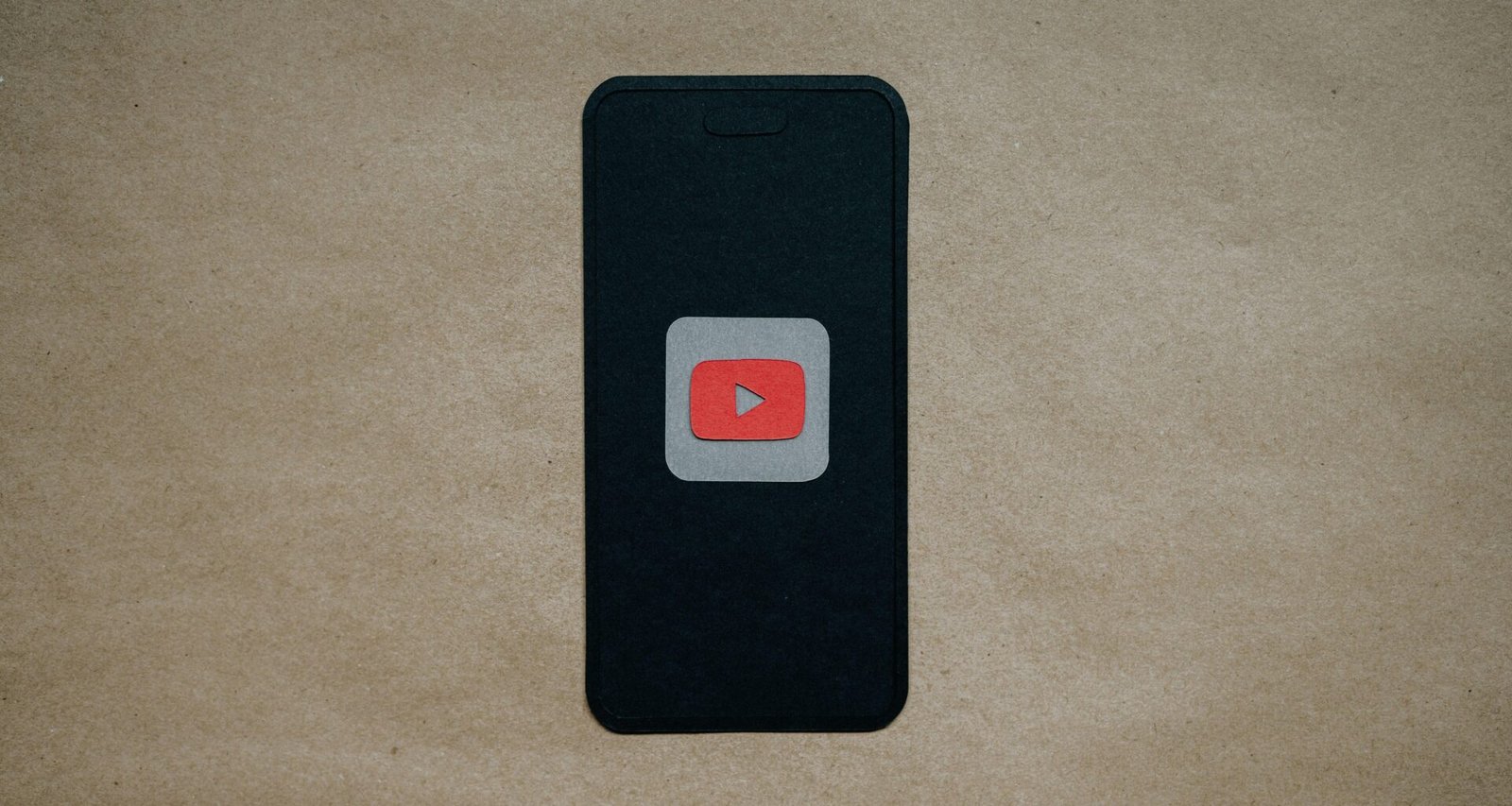 Schwarzes Smartphone mit prominentem roten YouTube-Logo auf dem Display, auf dunklem Hintergrund liegend